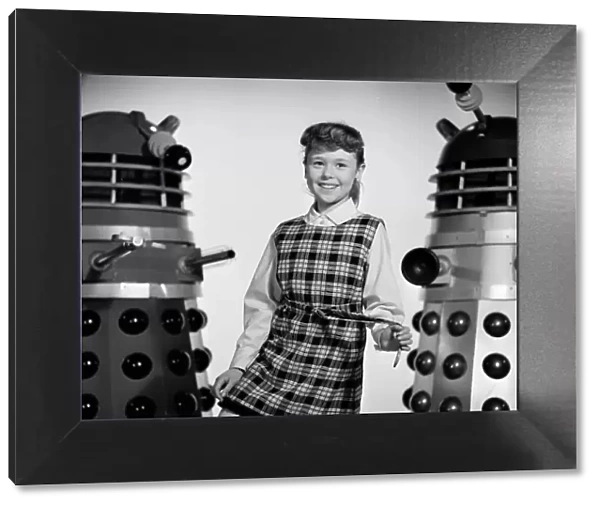 A portrait of a smiling Roberta Tovey as Susan with Daleks
