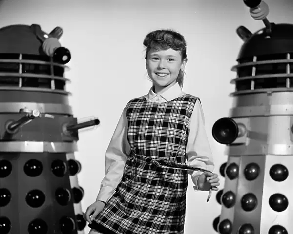 A portrait of a smiling Roberta Tovey as Susan with Daleks