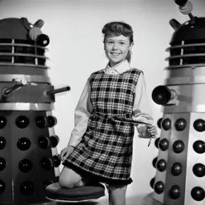 A portrait of a smiling Roberta Tovey as Susan with Daleks